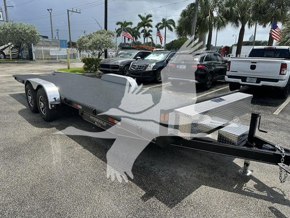 Flatbed trailer with dual axles and diamond plate toolbox on front, 2023 24 ft trailer in a dealership lot.