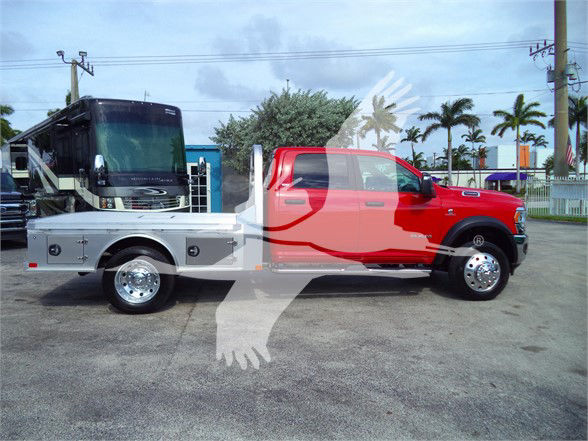 2023 Ram 5500 SLT flatbed truck side view showing red cab and silver flatbed with tool compartments and dual rear wheels.