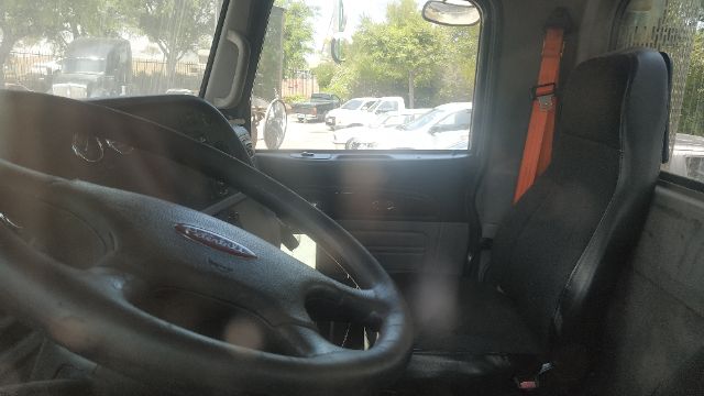 Peterbilt 386 truck interior showing steering wheel, driver seat, and orange seatbelt. Dashboard and window view of outdoor parking lot.