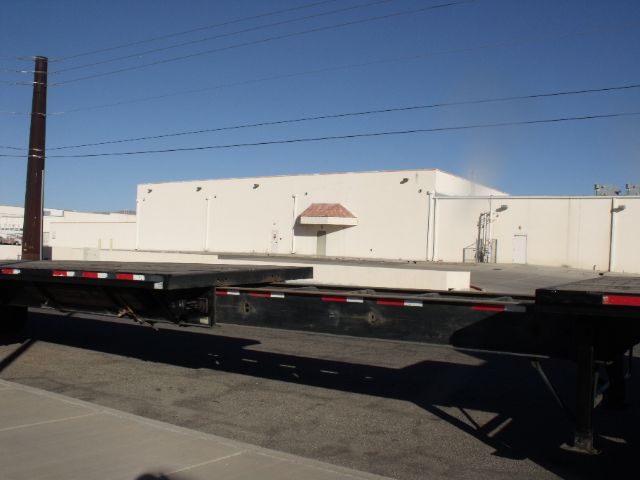 Flatbed expandable trailer with extendable sections, 48 to 80 foot, viewed from side. Background shows an industrial building.