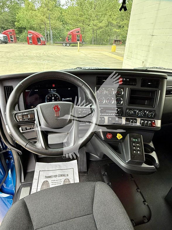 Kenworth T880 cockpit interior showing steering wheel, digital dash, center console with knobs, gear shifter, and left front seat with floor mat.