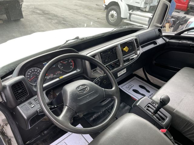 Box truck interior showing steering wheel, dashboard gauges, center console with gear shifter, and driver’s seat.