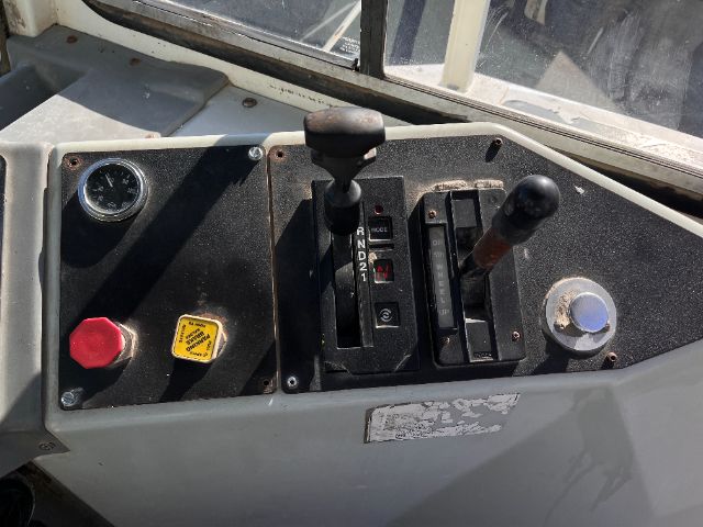 Operator cab panel with two gear levers, red emergency stop button, yellow warning sticker, and gauges in a Kalmar Ottawa truck.