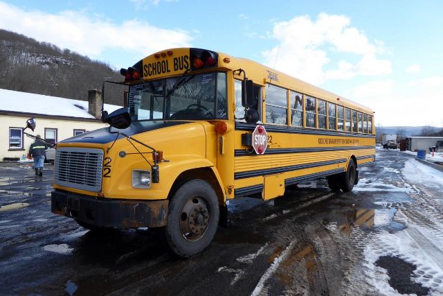 2002 Freightliner FS65 school bus in yellow with black trim, front grille, large mirrors, stop sign, and school bus signage.