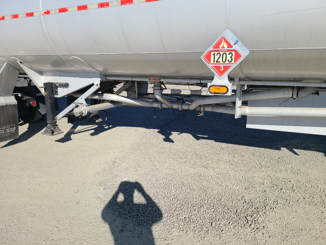Trailer underside showing piping, support beams, and a hazardous material placard with 1203 on a Beall semi trailer.