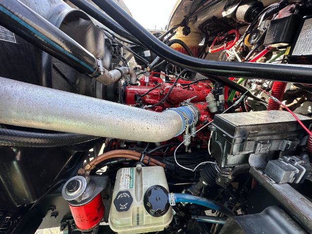 Truck engine bay showing red engine block, large silver intake pipe, coolant reservoir with blue hose, and various black boxes and wiring.