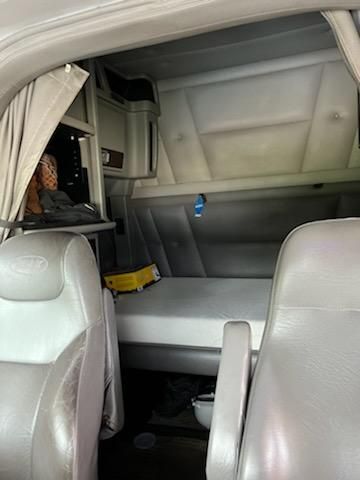 Trucking cab interior showing sleeper area with bed and storage, Peterbilt branding on seat headrest, various compartments and a yellow tool or object on bed.