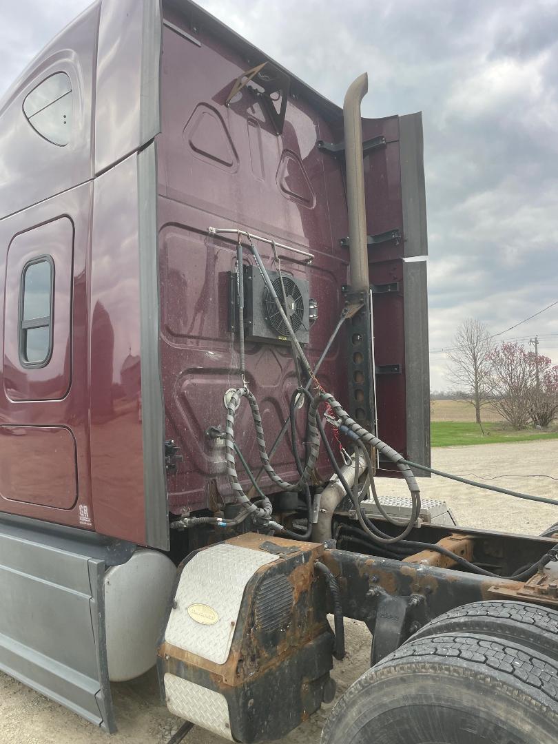 Truck cab area showing engine bay access from behind, with exposed wiring harnesses, air conditioning condenser, exhaust stack, and rusted fuel/air tanks near the rear wheel.