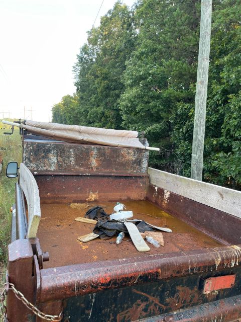 Dump truck bed with rusted metal and chained towing hooks, a tarp rolled up, and a wooden tailgate edge visible.