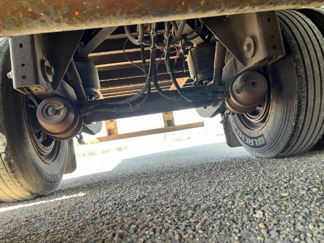 Rear undercarriage of a trailer showing dual axles and wheels, suspension, and leaf springs with tires labeled 'DODGE' or similar, viewed from ground level.