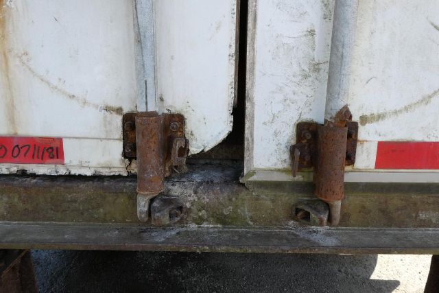 Trailer rear hinges and latches showing rusted hardware, white doors with red stock label, weathered bottom rail.