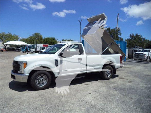 Ford F-250 dump bed truck in a parking lot, white exterior, mid-2010s model, dump bed raised at rear.
