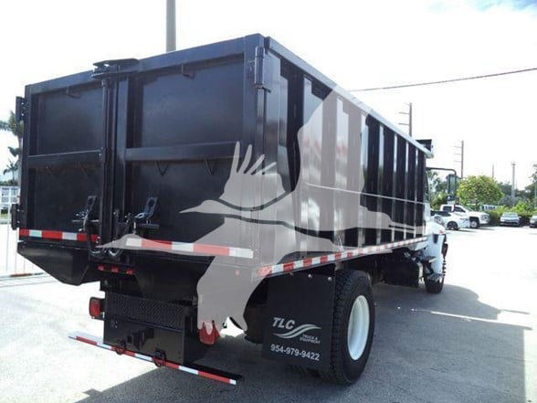 Dump truck rear and side view showing black dump body on a white-wheeled International Durastar 4300 with TLC logo and contact number on fender.