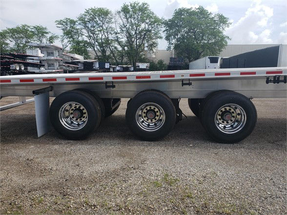 All-aluminum Fontaine REVOLUTION 52' flatbed trailer with triple axle wheels and reflective tape along the side.