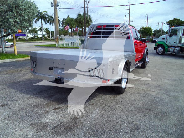 Ram 5500 flatbed truck rear view showing silver flatbed and red cab, stock number RAM5500LALSKCM visible, utility lights and hitch, dealership lot.
