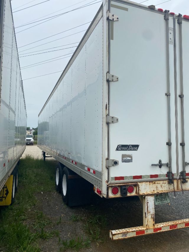 Trailer rear and side of a 2015 Wabash Duraplate box trailer, white exterior with rear doors, Great Dane logo sticker, rusted lower rear bumper, dual rear wheels visible.