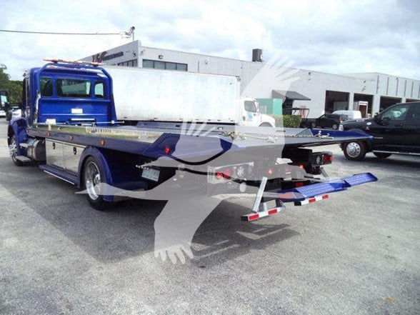 Kenworth T280 tow truck with flatbed, rear view showing loading ramp and trucks in background.
