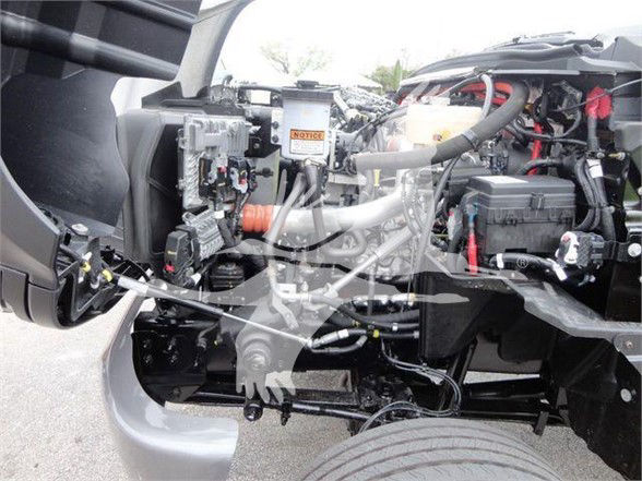 Truck engine bay showing various components including hoses, wiring, and a Power Steering Fluid/Reservoir area. Visible text areas include a small orange warning label and various stickers.
