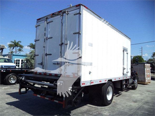 Rear view of a white refrigerated box truck with cargo doors open and a small side door. Concrete lot with palm trees in background.