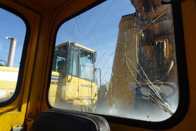Inside cab of a crane showing cracked windshield and another yellow Grove RT58 crane outside.