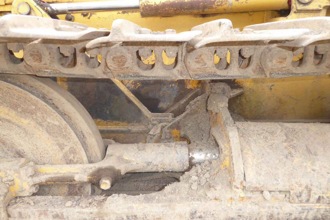 Underbody of a John Deere 650HLT tracked dozer showing sprockets, roller, and track drive components with dust and grime.