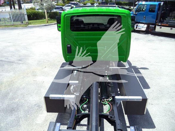Green tow truck cabin seen from rear with black hitch and wiring harness, coupler rails, and flatbed base.