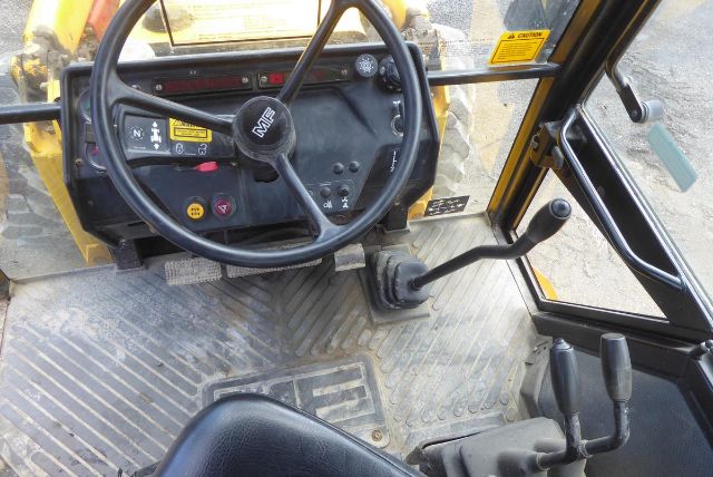 Massey Ferguson backhoe cab interior with steering wheel, control levers, and operator pedals.