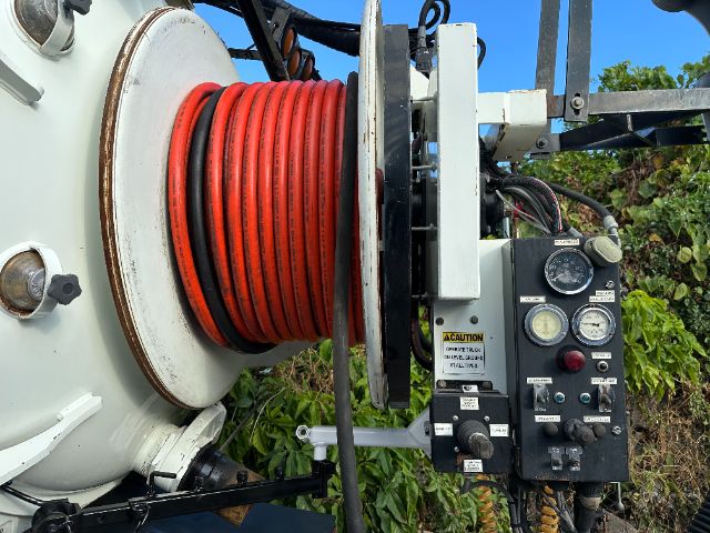Freightliner M2 vacuum truck winch reel with red hose and control panel showing gauges and warning label.