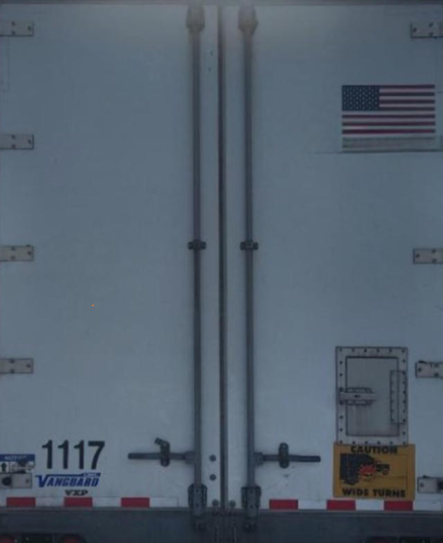 Back of a Vanguard VXP trailer with two rear doors, American flag sticker, stock number 1117, and 'Caution Wide Turns' sign.
