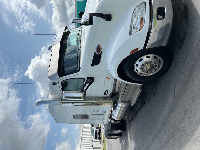 Peterbilt 579 truck in white, semi-tractor cab, side view with chrome exhaust stack, fuel tanks, and mirrors.