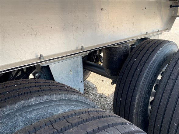 Trailer undercarriage showing dual tandem wheels and aluminum dump bed side with hinge area.