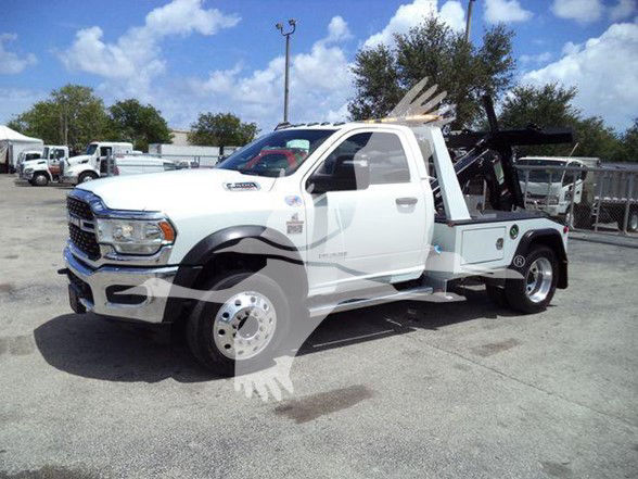 Ram tow truck with white cab and flatbed, front grille and RAM badge visible. No text clearly readable on panels due to image resolution.