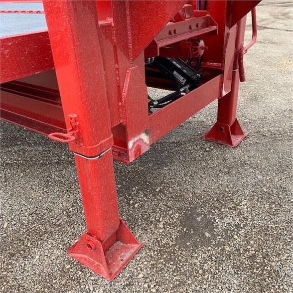 Single axle red drop deck container delivery trailer leg and undercarriage detail showing square mounting pads and structural rails.
