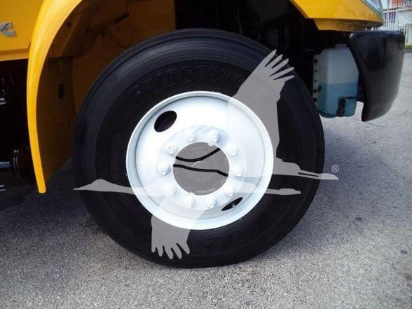 Wheel of a yellow dump truck showing a steel rim and tire, with part of the fender and blue coolant reservoir visible.