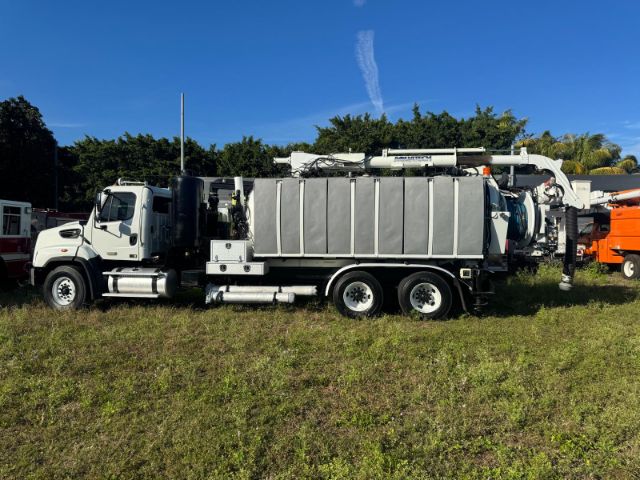 Freightliner 114SD vacuum truck side view with large silver compartments and mounted hose reels.