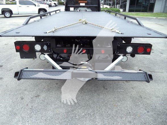 Rear view of a Freightliner Business Class M2 106 tow truck flatbed, showing tail lights, hitch area, and chain on the bed.