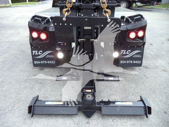 Freightliner Business Class M2 106 truck rear view showing hitch and equipment with lifting hooks and rear fender guards. Two red rear lights and TLC branding, contact number visible on mud flaps.