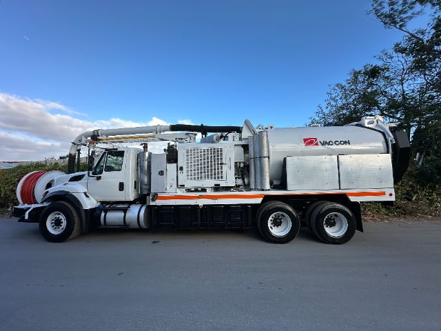 Vacuum truck from side view, 2016 International 7400, large rear tank with Vac-Con logo, hoses and piping along top, white cab with chrome mirrors, orange reflective stripe.