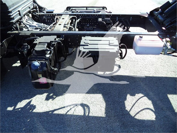 Isuzu NRR chassis frame with exposed cab-to-chassis area, visible battery, fluid reservoir, and wiring harnesses.