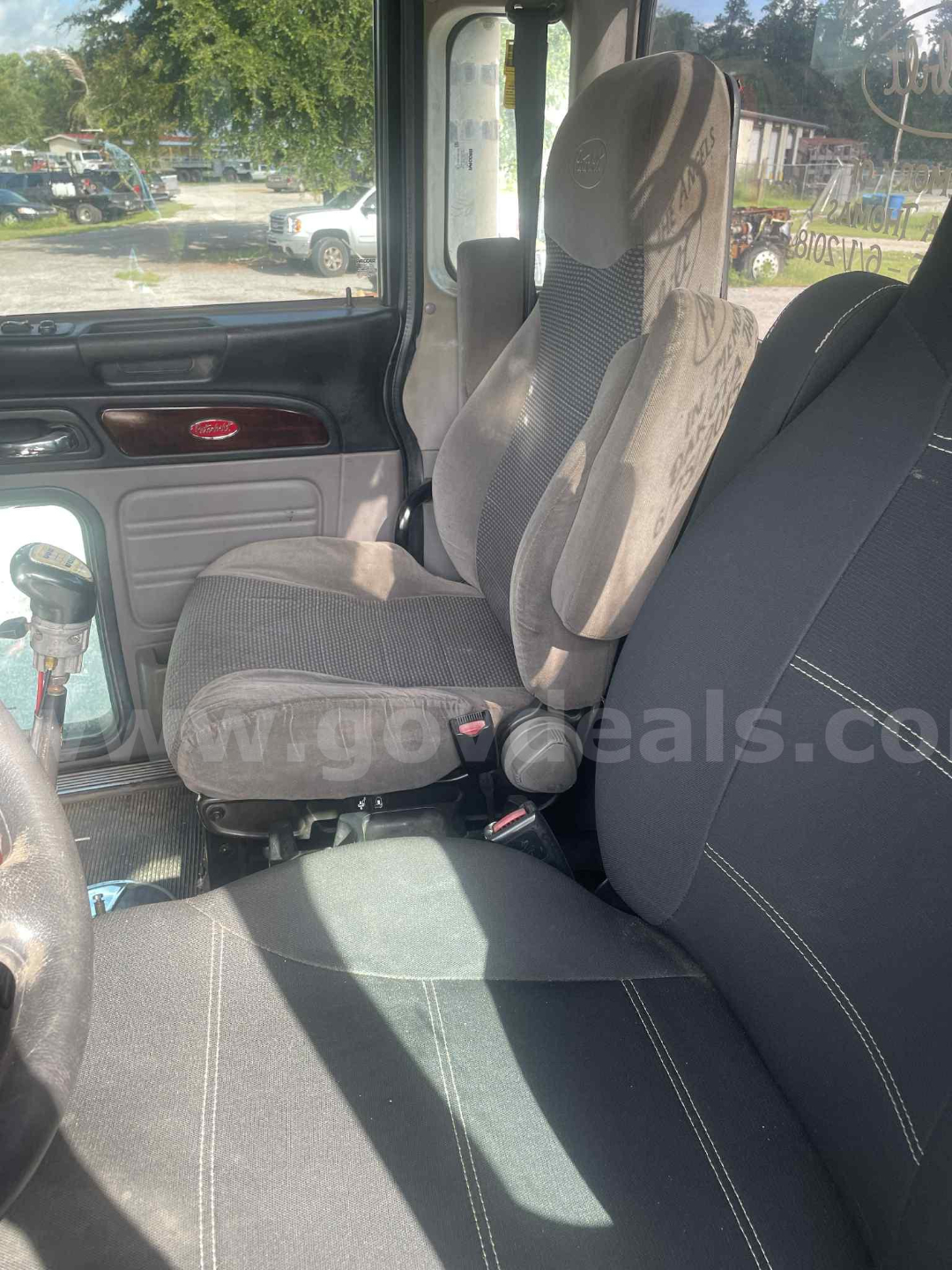 Cab interior of a 2012 Peterbilt 386 showing driver seat and passenger seat with fabric upholstery, steering wheel, window, and part of dashboard.