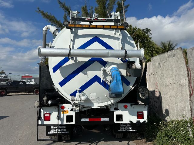 Vacuum truck rear view showing circular tank with blue diagonal stripe pattern, hoses, and rear lights.