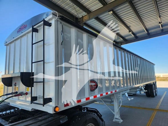 Hopper trailer with white cab and decorative graphic showing a deer silhouette, ladder on side, under a metal canopy.