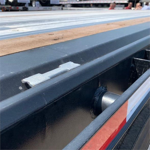 Flatbed trailer edge showing steel frame, roller guide, and side rail with reflective stripe.