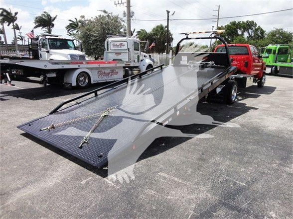 2023 International CV tow truck with a flatbed trailer and hydraulic tilt showing a long loading ramp and wheel-lift system. Tags include stock number and dealership lot in background.