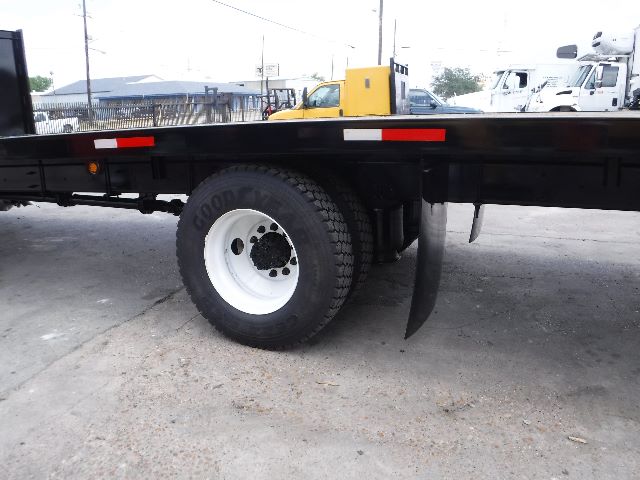 Flatbed truck image showing rear wheel and flatbed with a yellow cab in background. Visible text includes Goodyear tire brand on the tire sidewall.