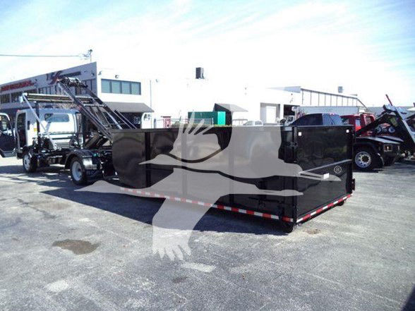 Isuzu NRR truck in yard with large black dump body, side view, dealership lot in background.