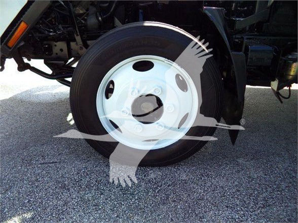 Isuzu NRR front wheel of a box truck showing steel white wheel and tire. Visible text on tire and surrounding chassis plates are not legible.