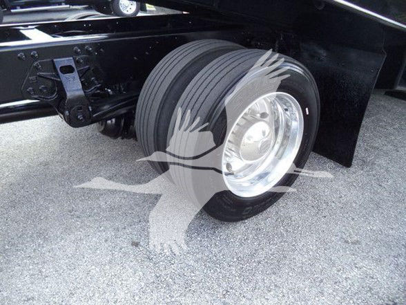 Truck wheel and suspension view on a 2014 Hino 258ALP tow truck, chrome wheel, black chassis, close-up of front axle and tire.
