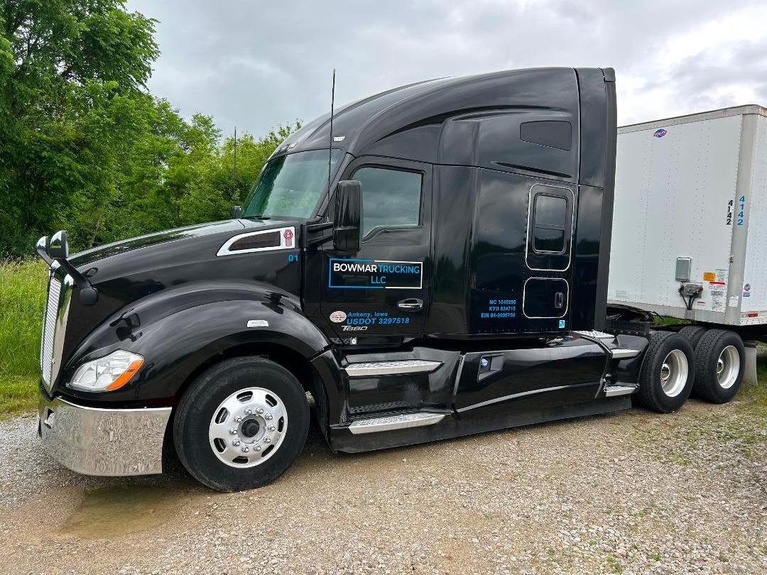 Kenworth T680 black tractor-trailer side view showing Bowmar Trucking LLC branding and service decals on door, fuel tanks, and chrome steps.