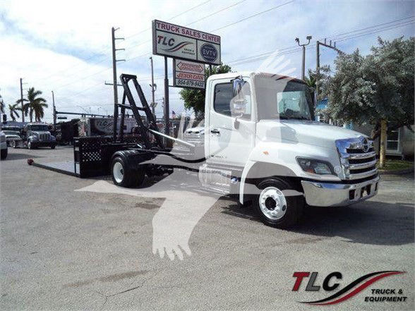 2017 Hino 258LP hooklift truck in a dealership lot, white cab with black hooklift apparatus and flatbed. TLC Truck & Equipment logo visible.
